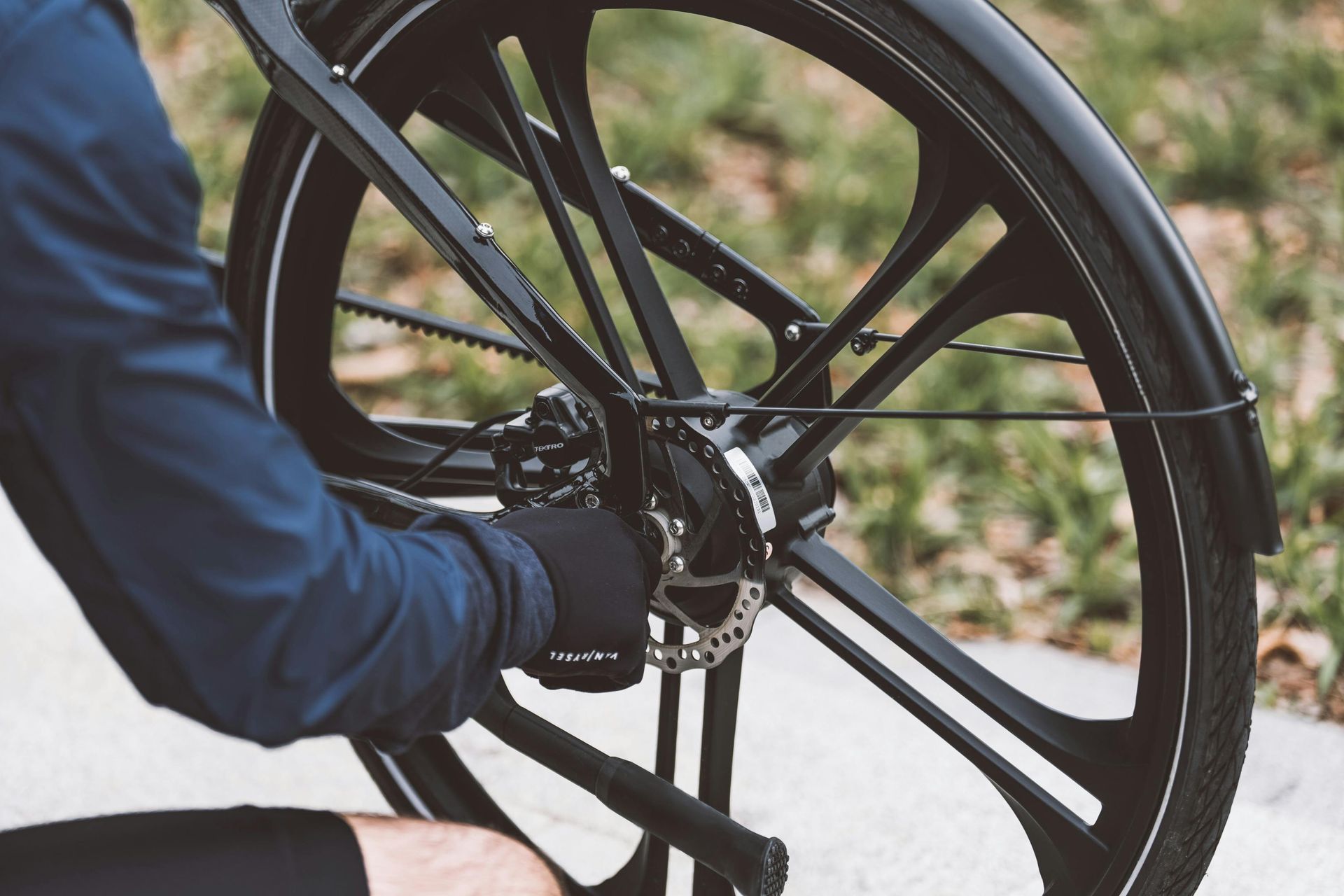 Person in black gloves working on a black bicycle's rear wheel, likely a repair.